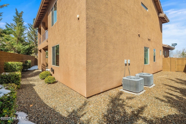 view of property exterior featuring cooling unit, stucco siding, and fence