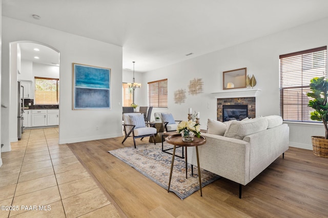 living room featuring a glass covered fireplace, arched walkways, light wood-style flooring, and baseboards