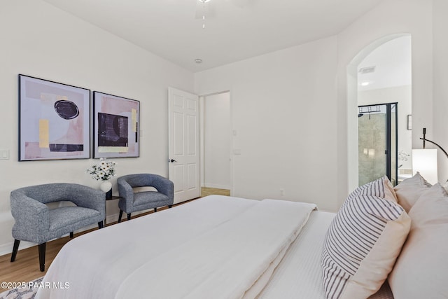 bedroom with arched walkways, wood finished floors, baseboards, and visible vents
