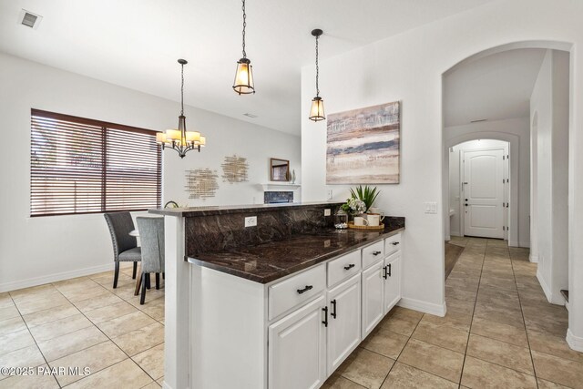 kitchen with light tile patterned floors, white cabinets, arched walkways, decorative light fixtures, and an inviting chandelier