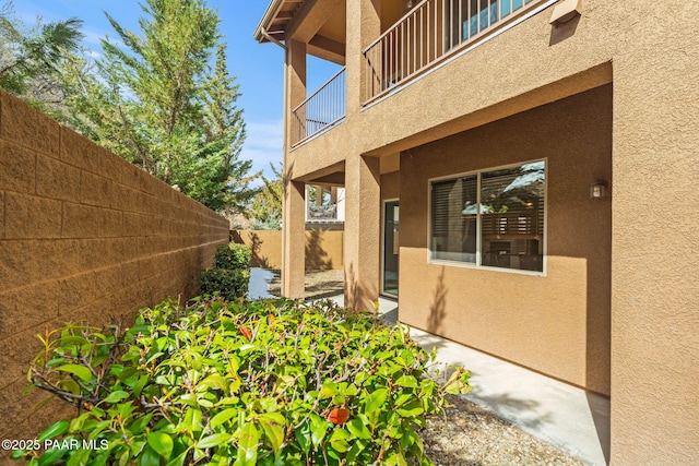 view of side of property with stucco siding, fence, and a balcony