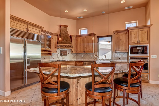 kitchen with custom range hood, built in appliances, a kitchen island, and a breakfast bar area