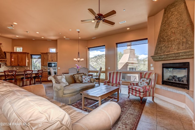 tiled living room featuring ceiling fan with notable chandelier and a large fireplace