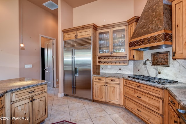 kitchen with tasteful backsplash, dark stone countertops, light tile patterned flooring, custom range hood, and appliances with stainless steel finishes