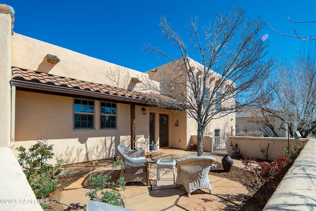 rear view of house featuring a gate, fence, stucco siding, a tiled roof, and a patio area