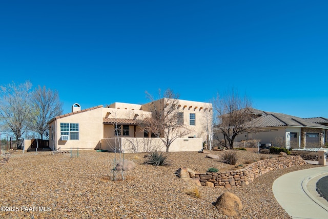 view of front of property featuring stucco siding, a tile roof, and fence