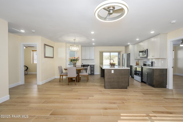 kitchen featuring stainless steel appliances, a center island, white cabinets, and decorative light fixtures