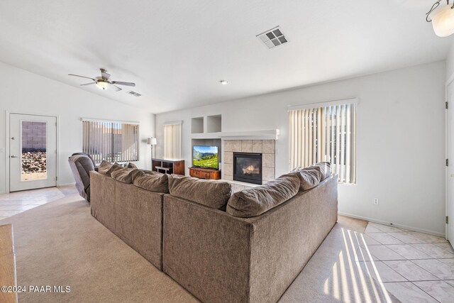 living room with a tiled fireplace, light tile patterned floors, a wealth of natural light, and vaulted ceiling