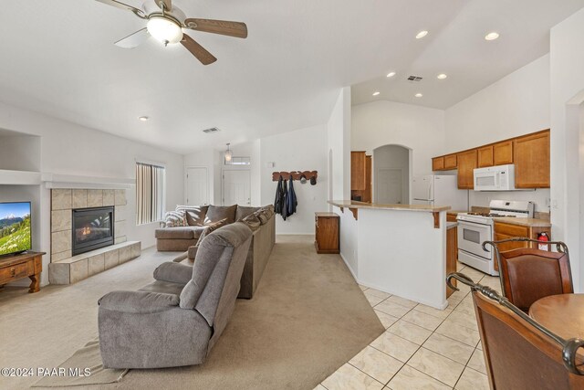 carpeted living room with vaulted ceiling, ceiling fan, and a tiled fireplace