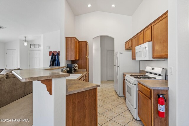 kitchen with kitchen peninsula, a kitchen bar, white appliances, vaulted ceiling, and light tile patterned floors