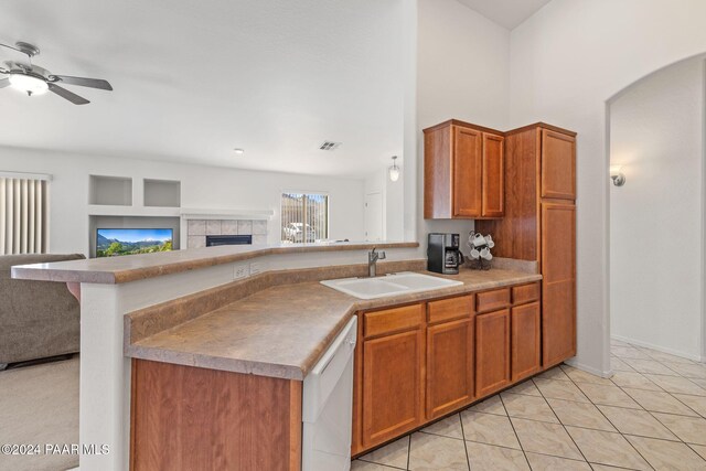 kitchen featuring white dishwasher, sink, ceiling fan, light tile patterned floors, and a tiled fireplace