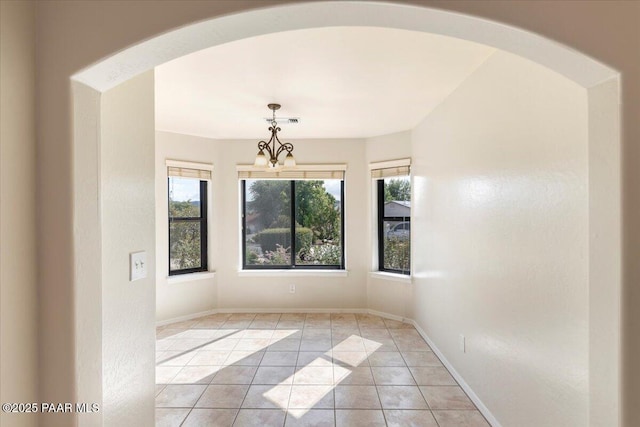 spare room featuring an inviting chandelier, a healthy amount of sunlight, and light tile patterned flooring