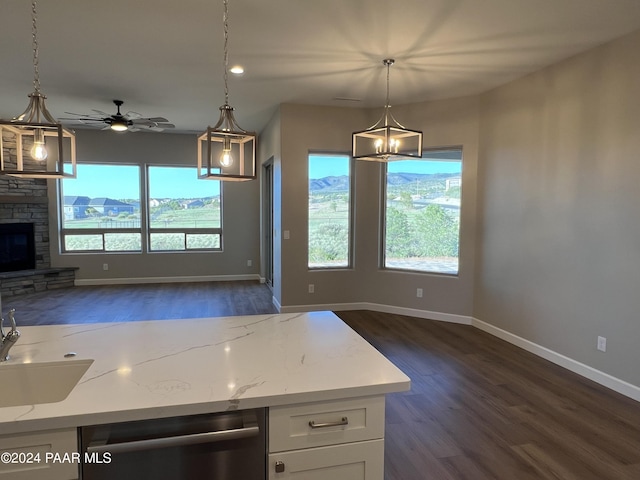 kitchen with light stone countertops, white cabinetry, hanging light fixtures, stainless steel dishwasher, and dark hardwood / wood-style floors