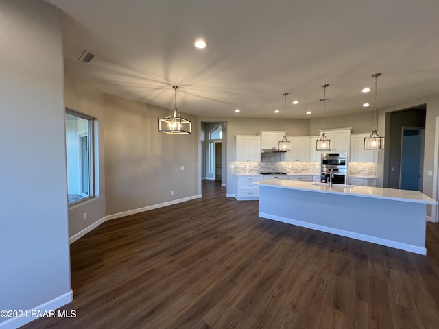 kitchen with dark hardwood / wood-style flooring, decorative light fixtures, white cabinetry, and a center island with sink