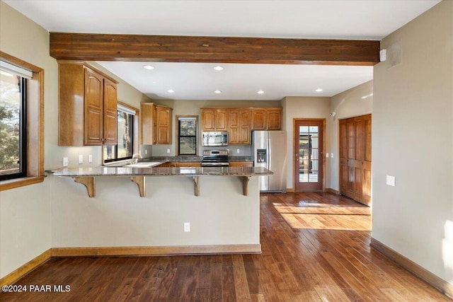 kitchen featuring kitchen peninsula, a kitchen breakfast bar, stainless steel appliances, dark stone countertops, and dark hardwood / wood-style floors