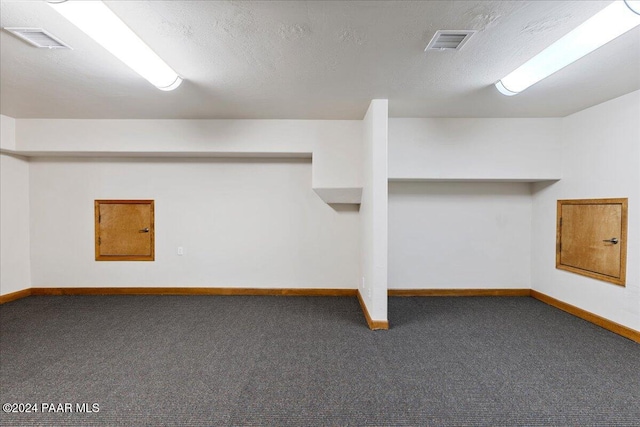 basement featuring a textured ceiling and dark colored carpet