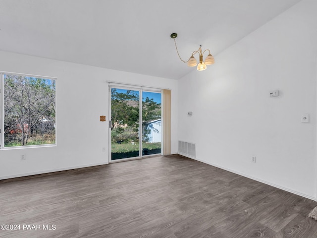 empty room featuring vaulted ceiling, an inviting chandelier, and dark wood-type flooring