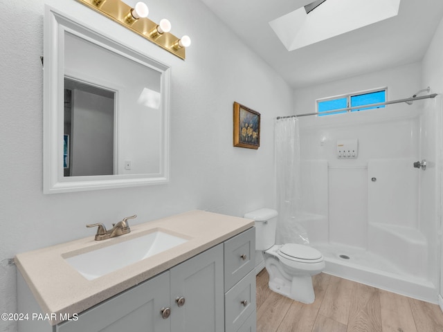 bathroom with a shower with shower curtain, a skylight, vanity, hardwood / wood-style floors, and toilet