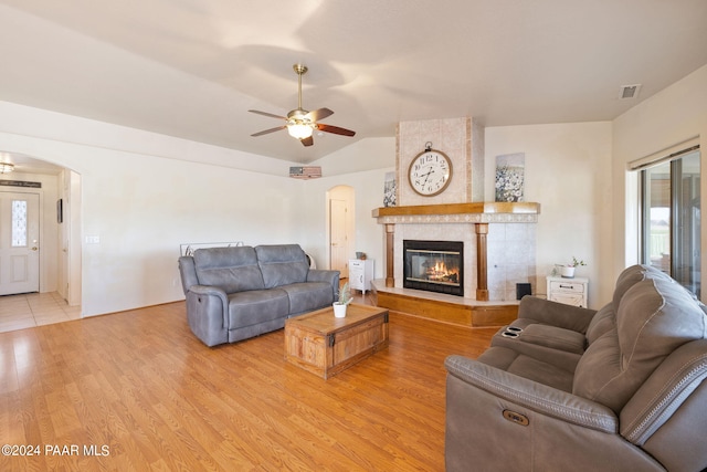 living room with ceiling fan, a fireplace, vaulted ceiling, and light wood-type flooring