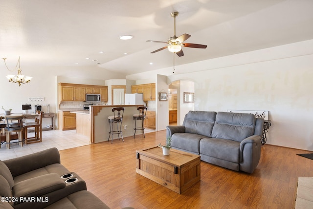 living room featuring ceiling fan with notable chandelier, light wood-type flooring, and vaulted ceiling