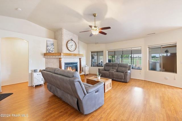 living room with ceiling fan, light wood-type flooring, a tile fireplace, and vaulted ceiling