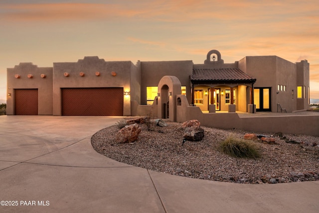 pueblo revival-style home with a garage, concrete driveway, a tiled roof, and stucco siding