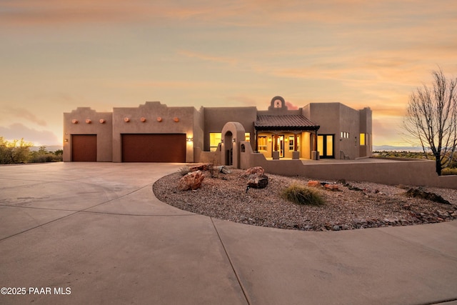 pueblo-style home with a garage, concrete driveway, and stucco siding