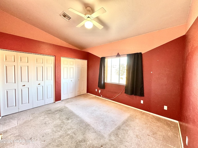 unfurnished bedroom featuring ceiling fan, vaulted ceiling, carpet floors, and two closets