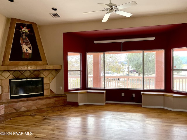 unfurnished living room with a stone fireplace, ceiling fan, and light hardwood / wood-style flooring