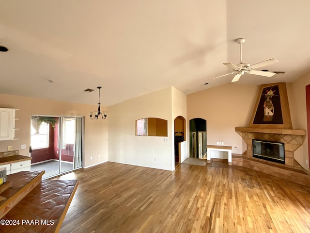 unfurnished living room featuring a tile fireplace, hardwood / wood-style floors, ceiling fan with notable chandelier, and vaulted ceiling