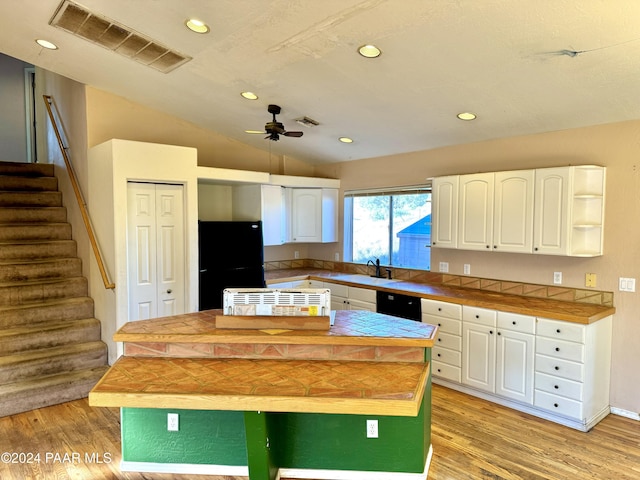 kitchen with lofted ceiling, white cabinets, black appliances, light wood-type flooring, and a kitchen island