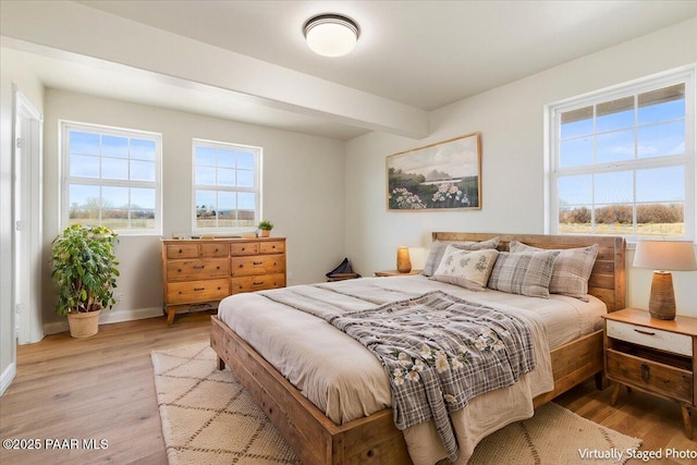 bedroom featuring light wood finished floors, baseboards, and beam ceiling