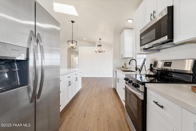 kitchen with a sink, white cabinetry, vaulted ceiling, appliances with stainless steel finishes, and pendant lighting