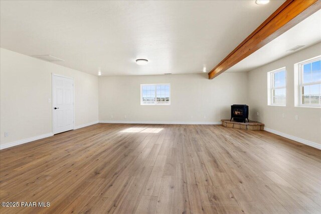 unfurnished living room featuring visible vents, baseboards, light wood-type flooring, beam ceiling, and a wood stove