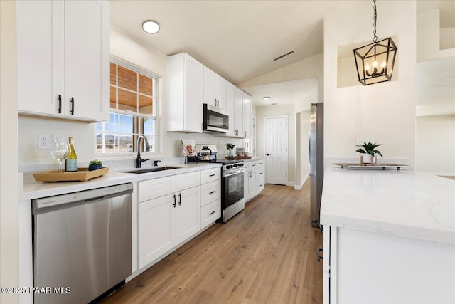 kitchen with stainless steel appliances, lofted ceiling, hanging light fixtures, white cabinets, and a sink