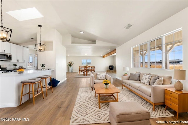 living area with light wood finished floors, visible vents, baseboards, lofted ceiling with skylight, and an inviting chandelier