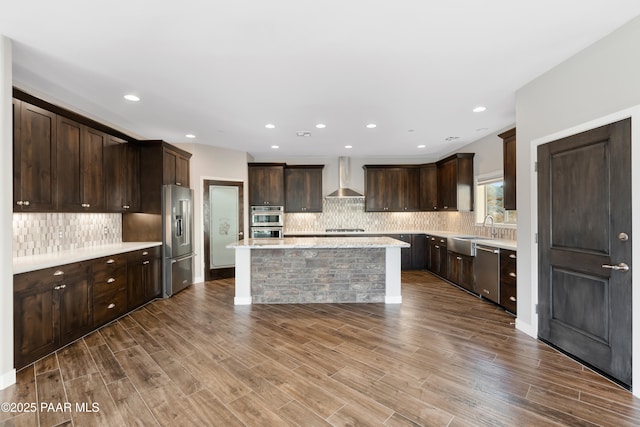 kitchen with a center island, wall chimney range hood, light wood-type flooring, appliances with stainless steel finishes, and dark brown cabinetry