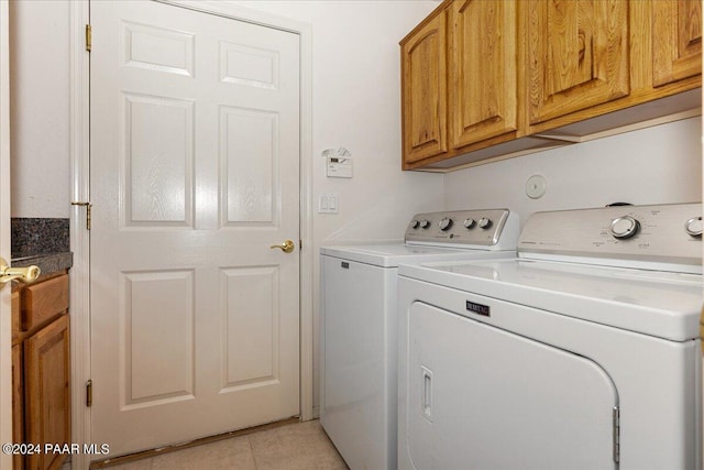 clothes washing area with light tile patterned flooring, cabinets, and washing machine and clothes dryer