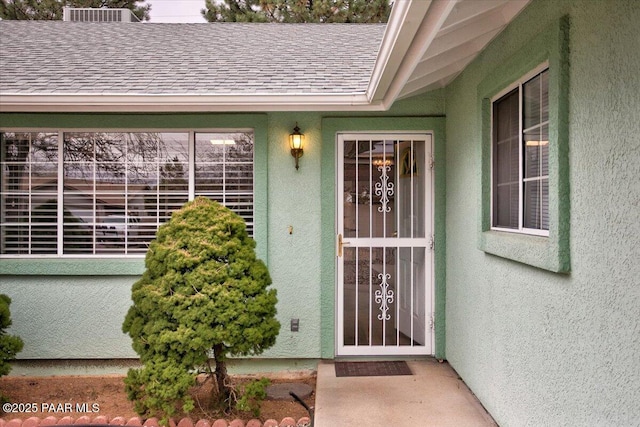 view of exterior entry with roof with shingles and stucco siding