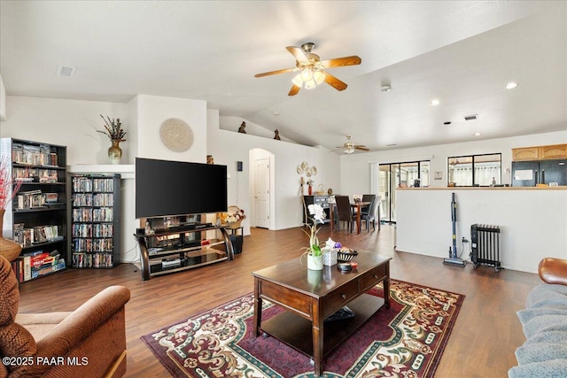 living area with ceiling fan, arched walkways, vaulted ceiling, wood finished floors, and radiator heating unit