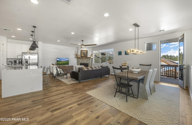 dining space featuring visible vents, ceiling fan with notable chandelier, a glass covered fireplace, recessed lighting, and light wood-style floors