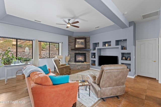 living area with built in features, visible vents, a stone fireplace, and ceiling fan