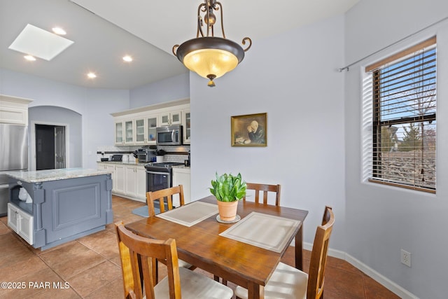 dining room featuring baseboards, light tile patterned floors, recessed lighting, a skylight, and arched walkways