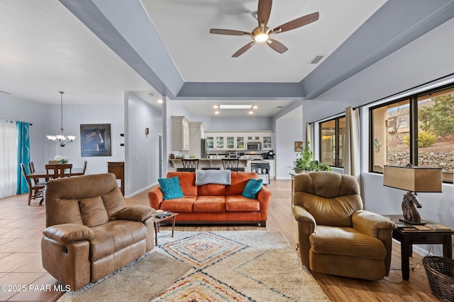 living room with light tile patterned floors, visible vents, ceiling fan with notable chandelier, and baseboards