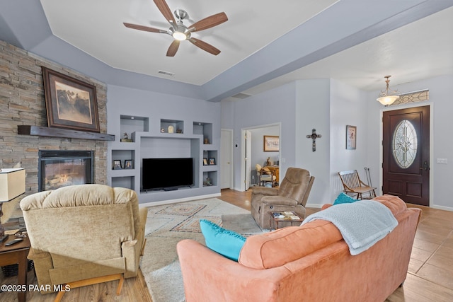 living room featuring visible vents, built in features, a fireplace, baseboards, and ceiling fan