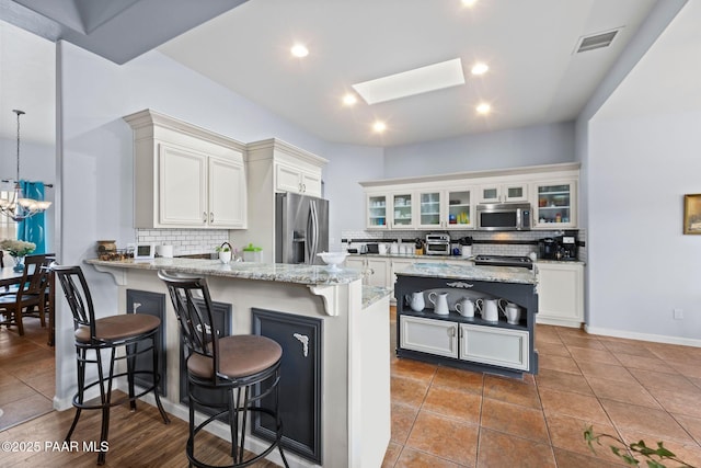 kitchen featuring visible vents, light stone countertops, a breakfast bar area, a peninsula, and stainless steel appliances