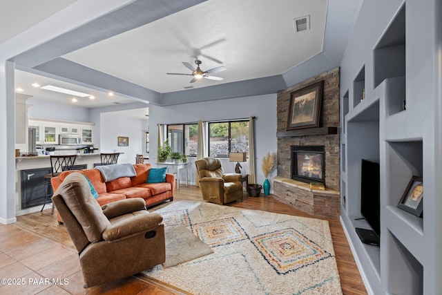 living room featuring visible vents, a fireplace, light wood-style floors, and ceiling fan