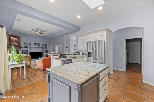 kitchen featuring a ceiling fan, white cabinetry, stainless steel appliances, a peninsula, and light stone countertops