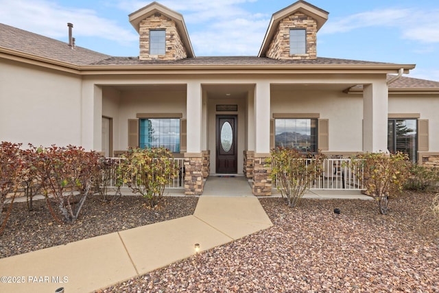 doorway to property featuring covered porch, stone siding, and stucco siding