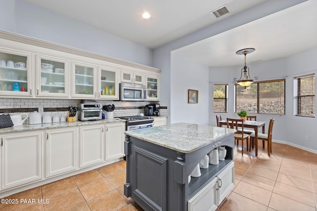 kitchen with light tile patterned floors, stainless steel microwave, backsplash, and visible vents